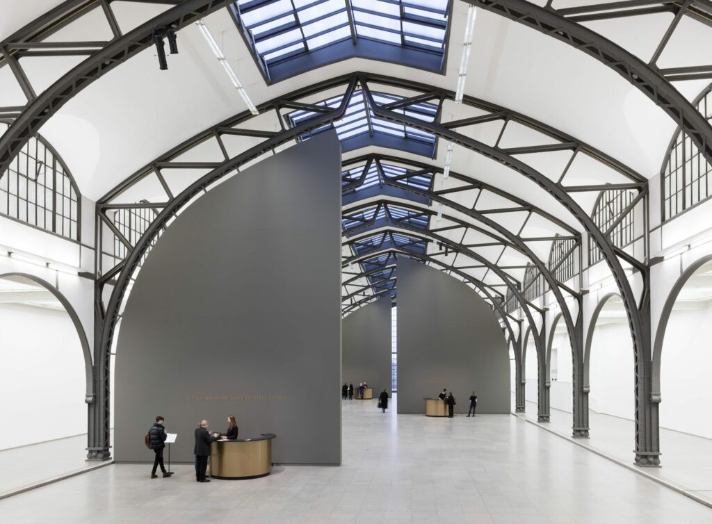 Adrian Piper, The Probable Trust Registry: The Rules of the Game #1-3, 2013-2017, Installation + Group Performance: 3 grey walls reaching from floor to the ceiling, 3 golden circular desks, golden embossed letters, 3 standing desks, 3 lean stools, computer system, 3 receptionists (one behind each desk). Adaptable Dimensions. Detail: The Rules of the Game #1. Staatliche Museen zu Berlin, Nationalgalerie / Thomas Bruns. Sammlung Staatliche Museen zu Berlin, Nationalgalerie. 2016 Schenkung der Freunde der Nationalgalerie. © Adrian Piper Research Archive Foundation Berlin. © APRA Foundation Berlin