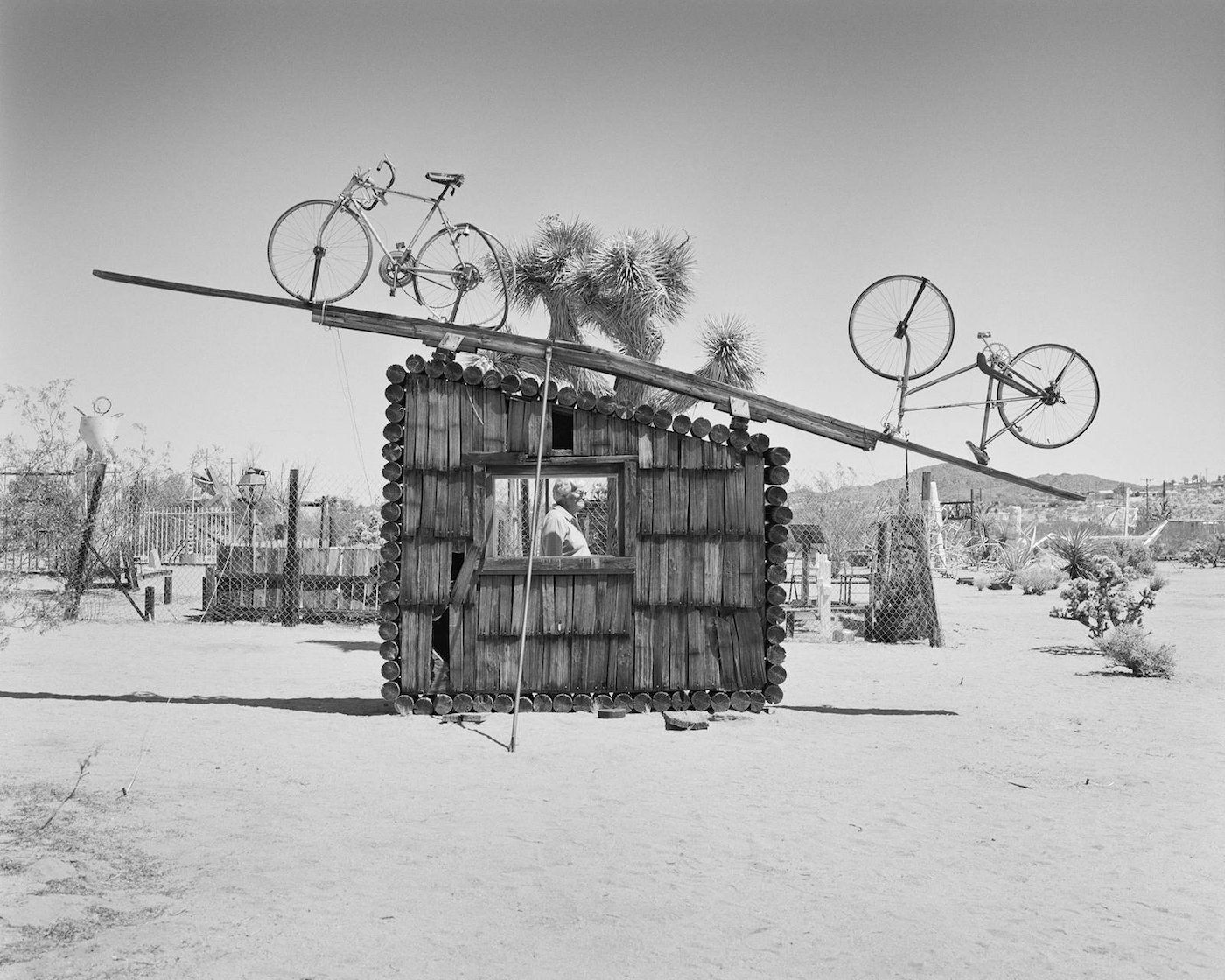LaToya Ruby Frazier, Pat Brunty, the caretaker standing behind No Contest 1994, Noah Purifoy Outdoor Desert Art Museum, Joshua Tree, CA, Gelatin silver print (2017)