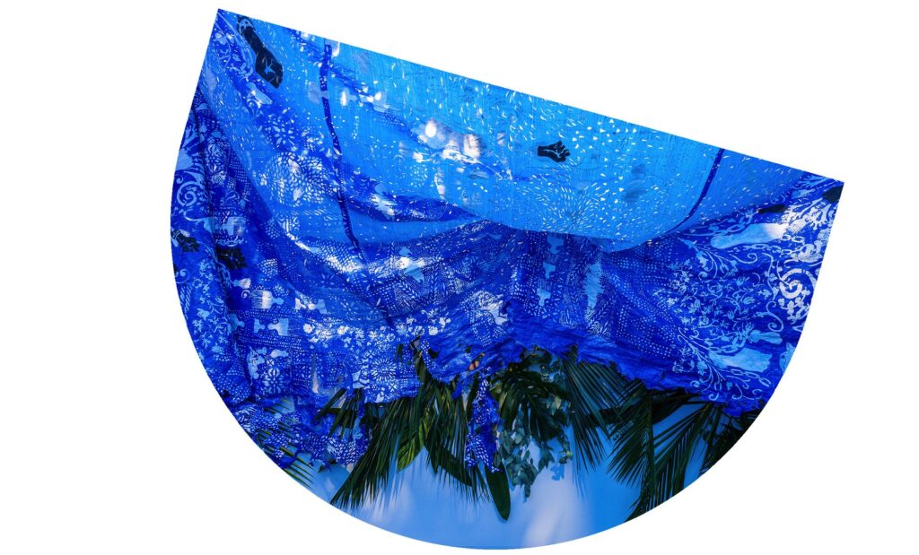 Firelei Báez, roots when they are young and most tender, 2018. Site-specific installation; two paintings, four–six hand-painted papier-mâché sculptures, 40 x 30 foot hand-painted blue tarp, chicken wire, and foliage. The Rennie Collection. Image courtesy of the artist, Kavi Gupta, Chicago, and James Cohan, New York. Photo: John Lusis.

